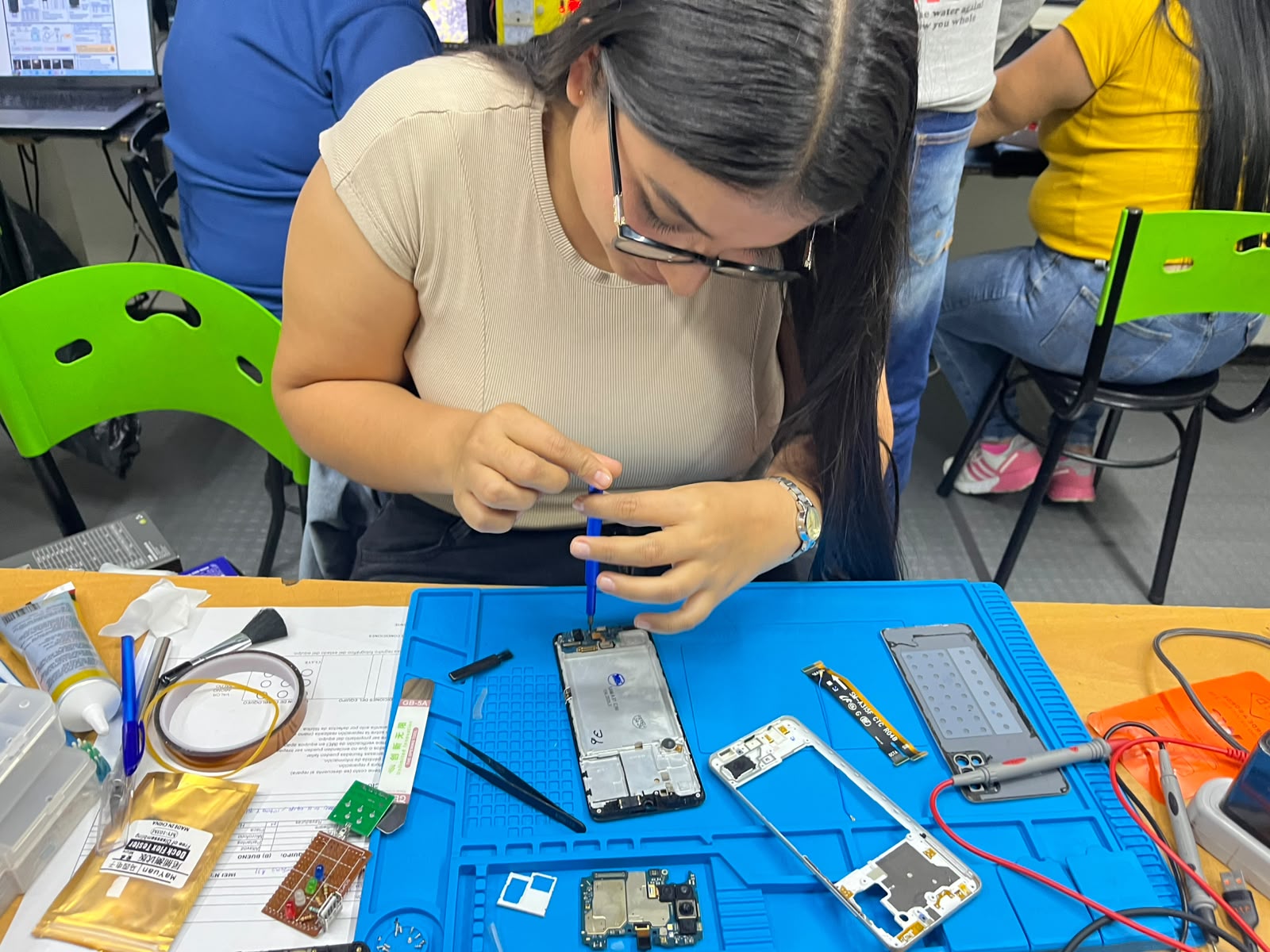 Estudiante desensamblando celular en clase práctica